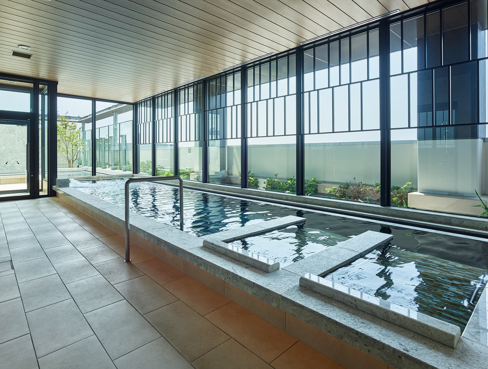 A large, serene public bath with clear water and wide windows that offer a view of the outside.