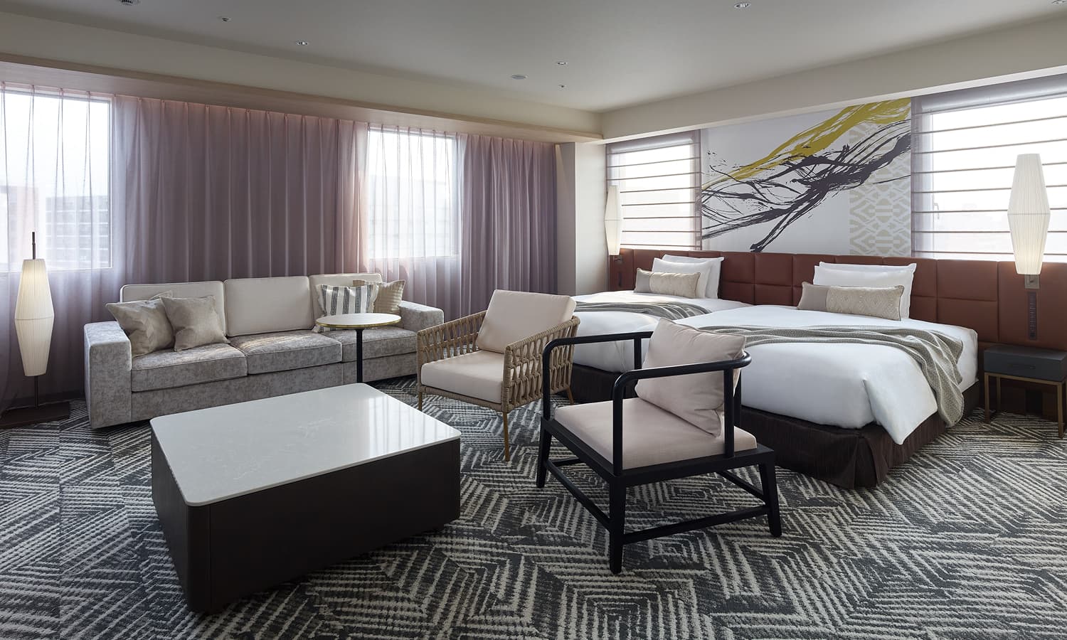 The Junior Suite , 2 beds room features two beds, a comfortable sofa, two armchairs, and abstract art above the beds.