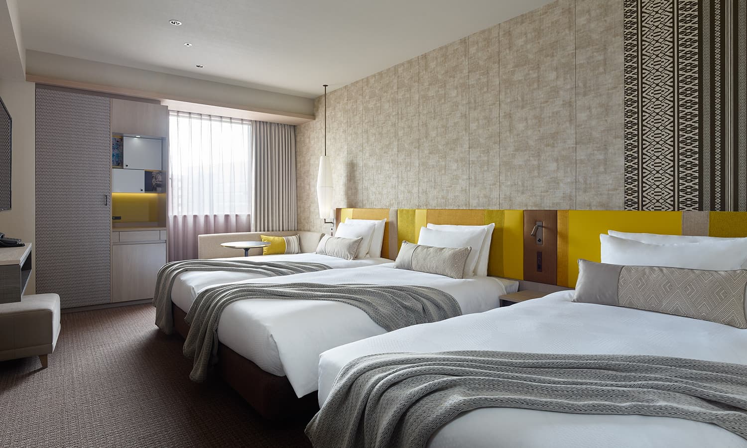 The Standard , 3 beds room features three single beds, each with a gray throw blanket, and a small sitting area by the window.