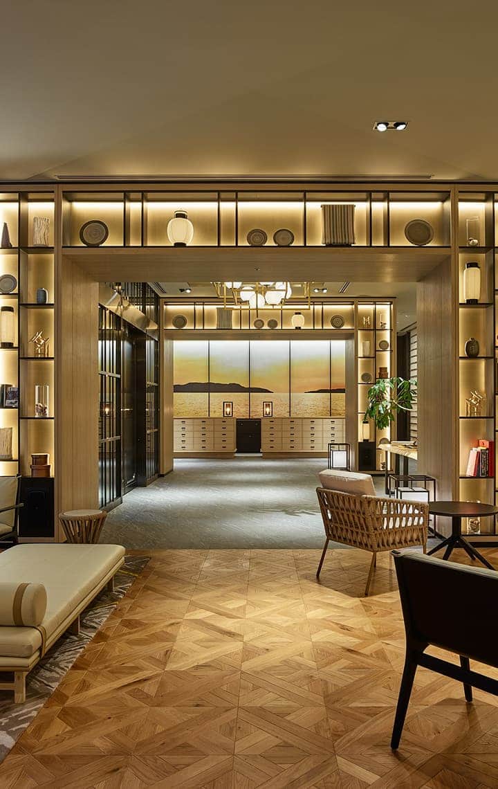 A luxurious hotel lobby with illuminated shelves displaying decorative items, comfortable seating, and a large mural of a sunset.