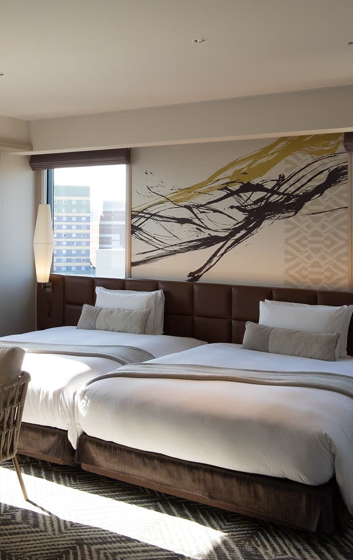 A hotel room featuring two comfortable beds, a plush sofa, an armchair, and windows with city views.