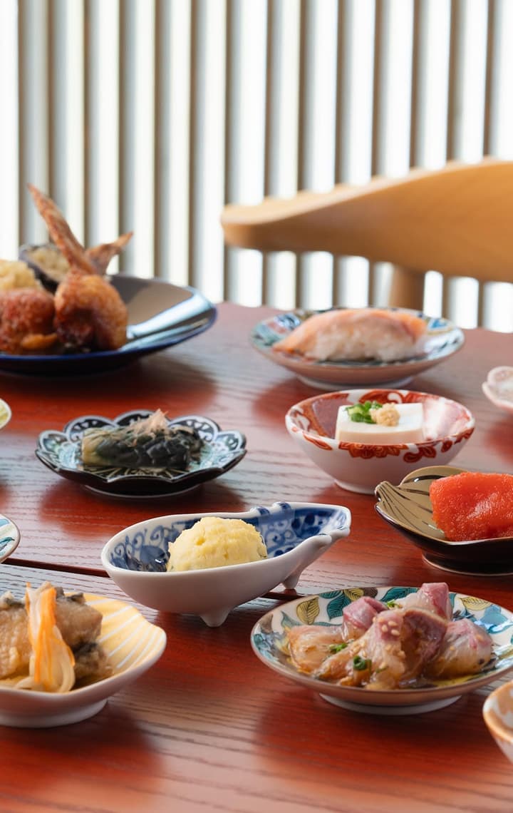 A vibrant spread of small Japanese dishes on a wooden table, including sushi, tempura, and various colorful appetizers.