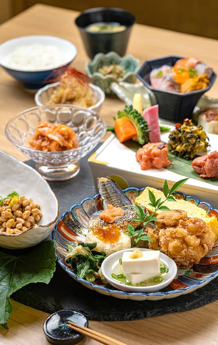 传统日本美食特写，包括米饭、味噌汤、烤鱼、炸鸡、纳豆等各色小菜。
