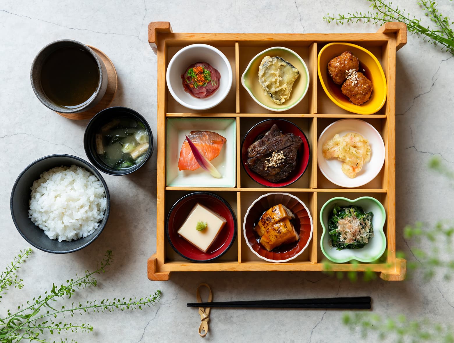 傳統日式早餐的俯瞰圖,木製便當盒中盛放九道小菜,搭配米飯、味噌湯和綠茶。