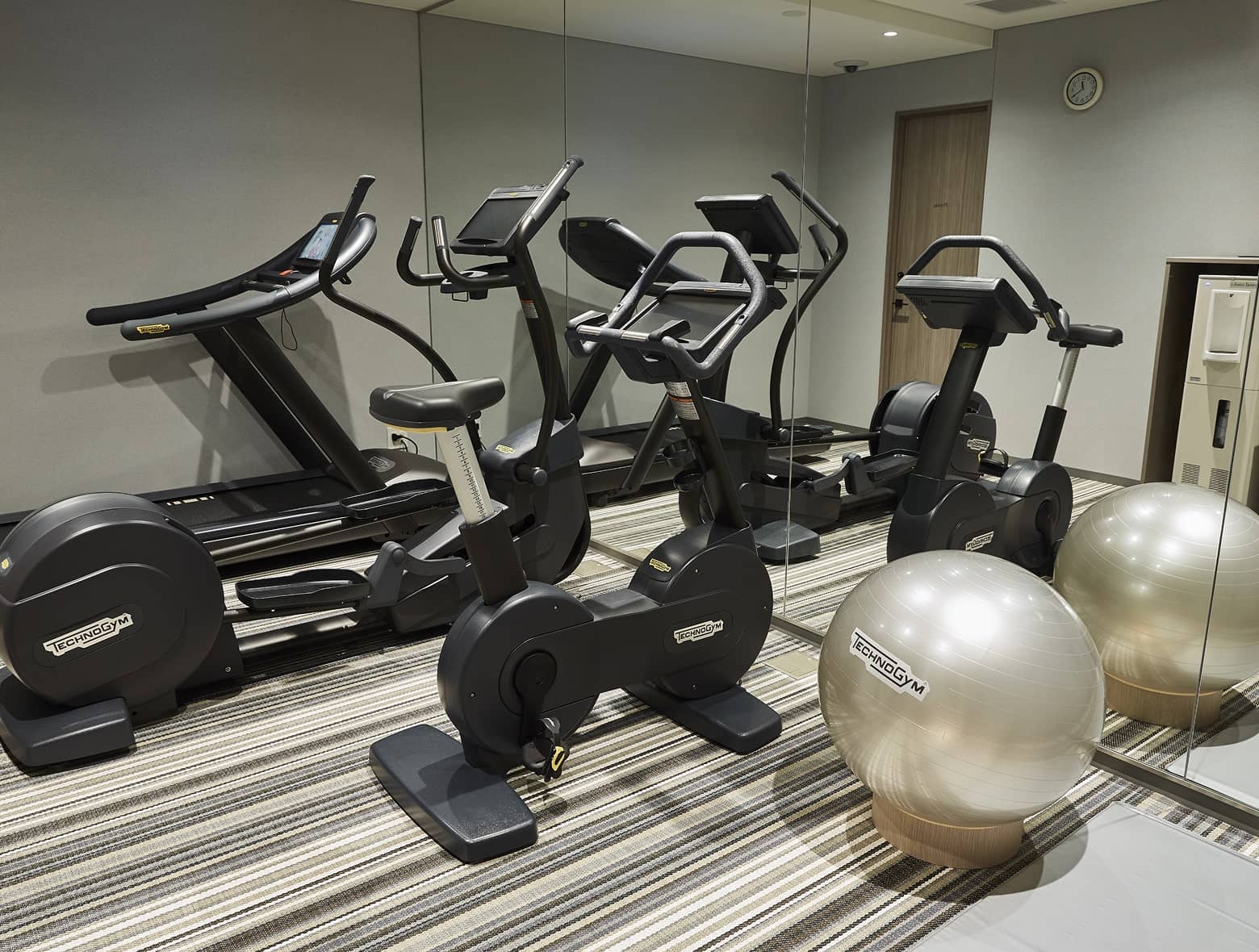 健身房的條紋地毯上有 Technogym 設備，包括健身腳踏車、跑步機和橢圓機。