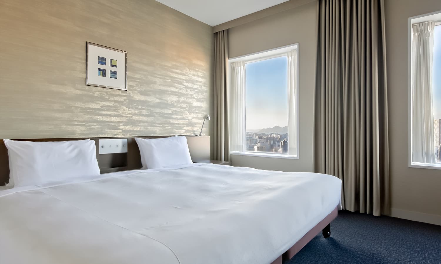 디럭스 킹룸에는 킹사이즈 침대, 카펫 바닥, 우드 소재 헤드보드, 독특한 질감의 벽지, 탁 트인 도시 전망을 감상할 수 있는 넓은 창이 있습니다.