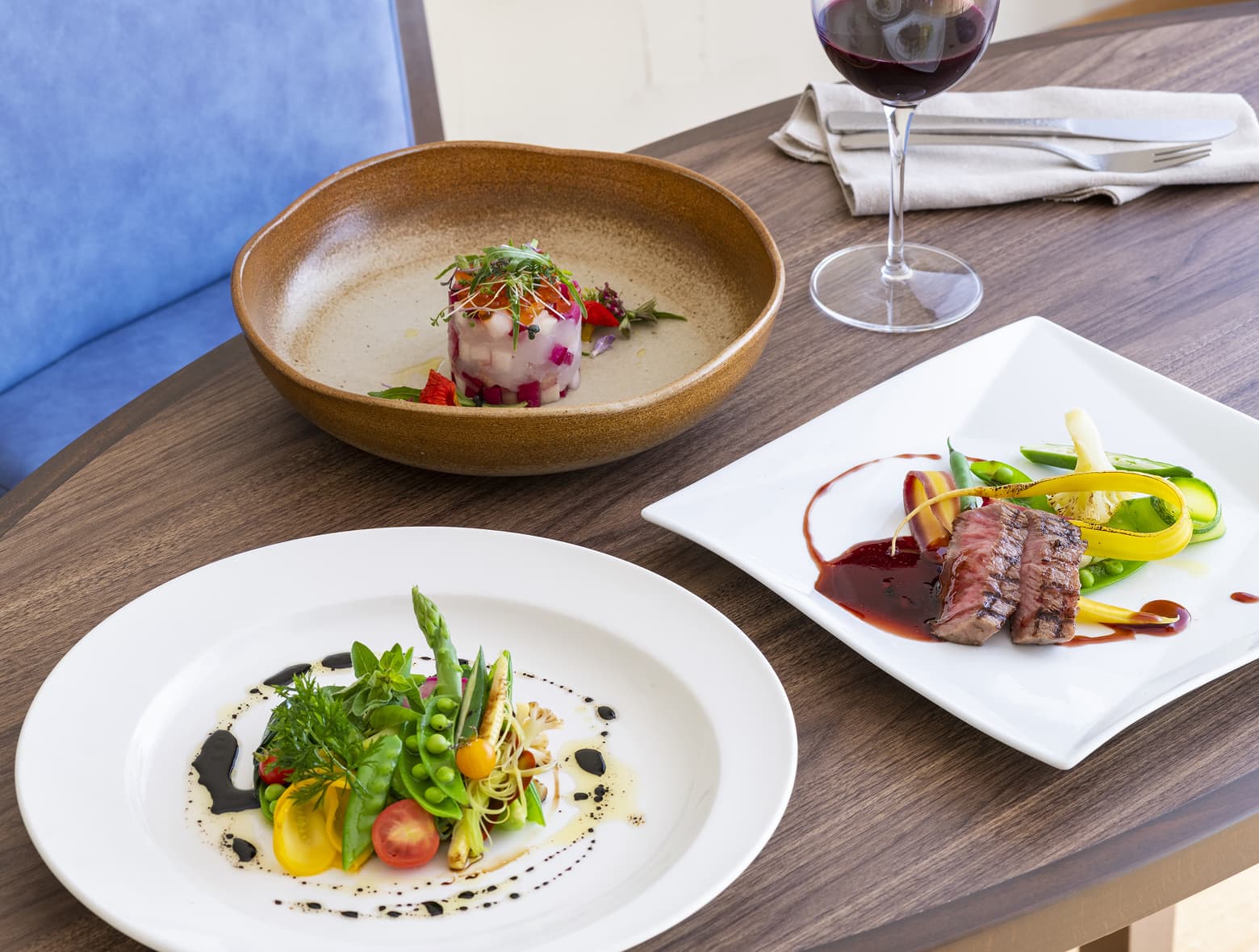 나무 테이블 위에 놓인 디너 메뉴. 멋지게 플레이팅된 야채 샐러드, 소스와 야채를 곁들인 스테이크, 전채 요리.