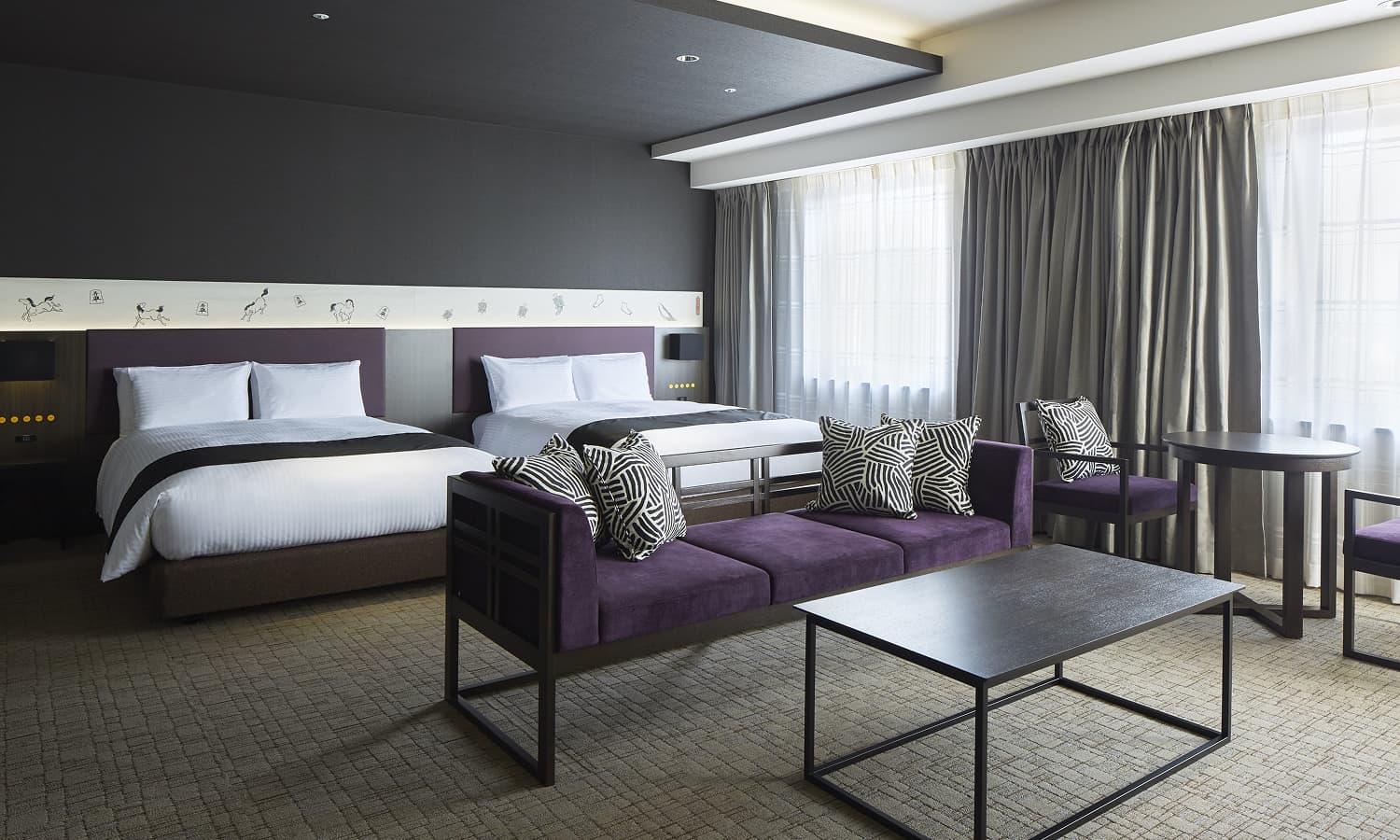 주니어 스위트 트윈룸은 싱글 침대 2개, 보라색 헤드보드, 짙은 보라색 벨벳 소파, 기하학적 패턴의 쿠션을 갖추고 있습니다.