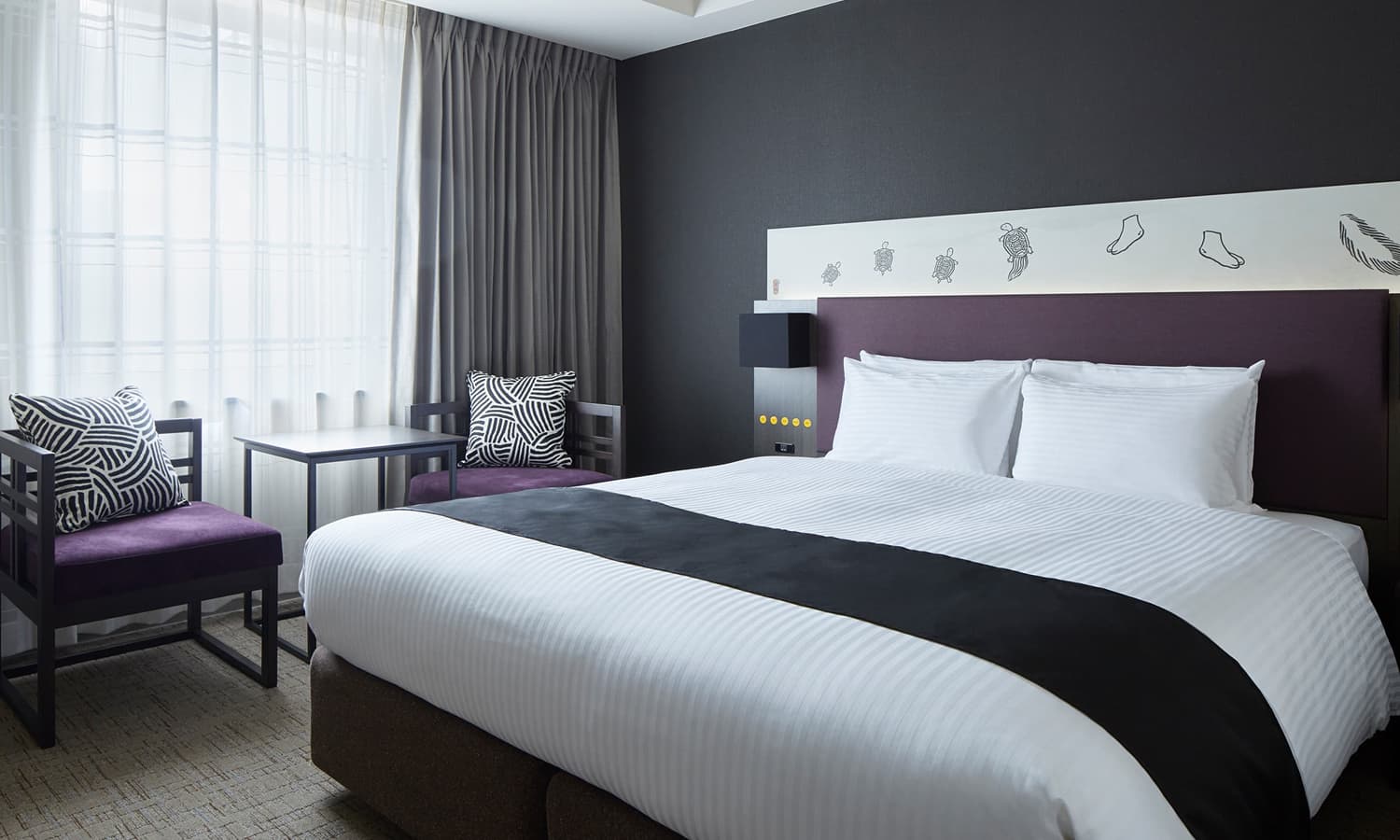 슈페리어 퀸룸은 보라색 벨벳 헤드보드가 있는 퀸 사이즈 침대와 보라색 의자가 놓인 창가 좌석 공간을 갖추고 있습니다.