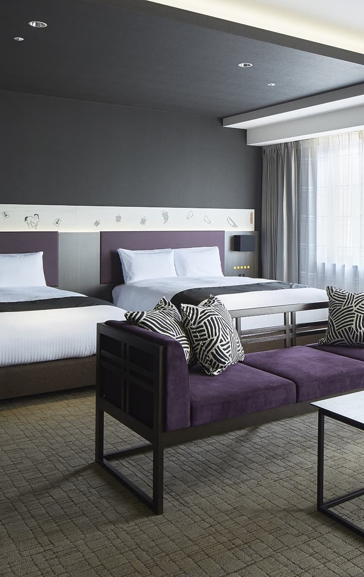 주니어 스위트 트윈룸은 보라색 헤드보드, 짙은 보라색 벨벳 소파, 기하학적 패턴의 쿠션을 갖추고 있습니다.