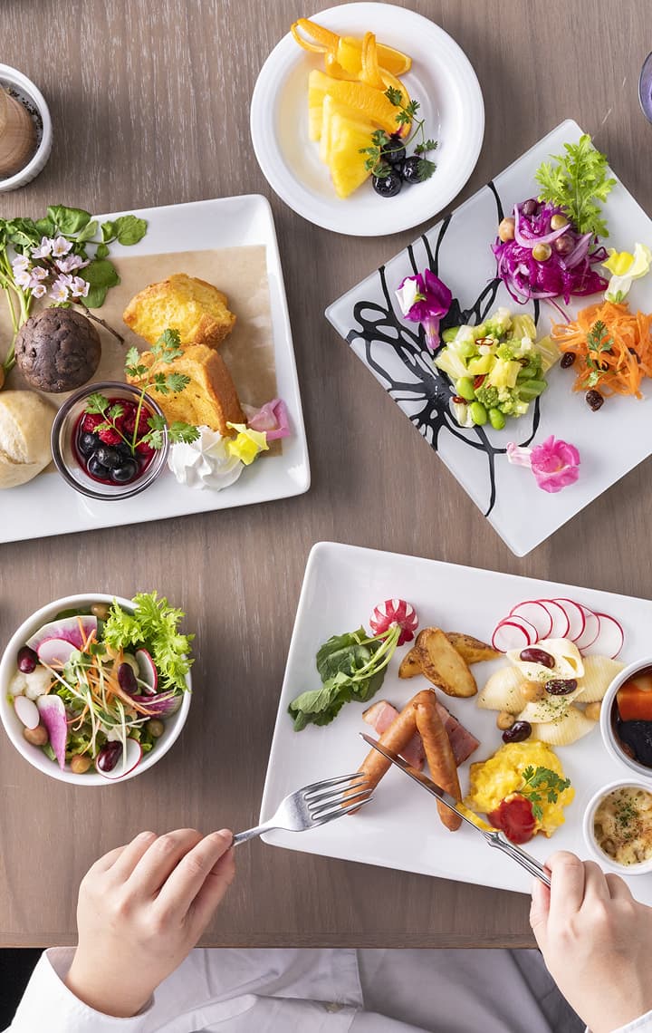 빵, 페이스트리, 다채로운 샐러드, 블랙커피 한 잔으로 구성된 아름다운 플레이팅의 다양한 아침 식사 메뉴를 위에서 바라본 모습.