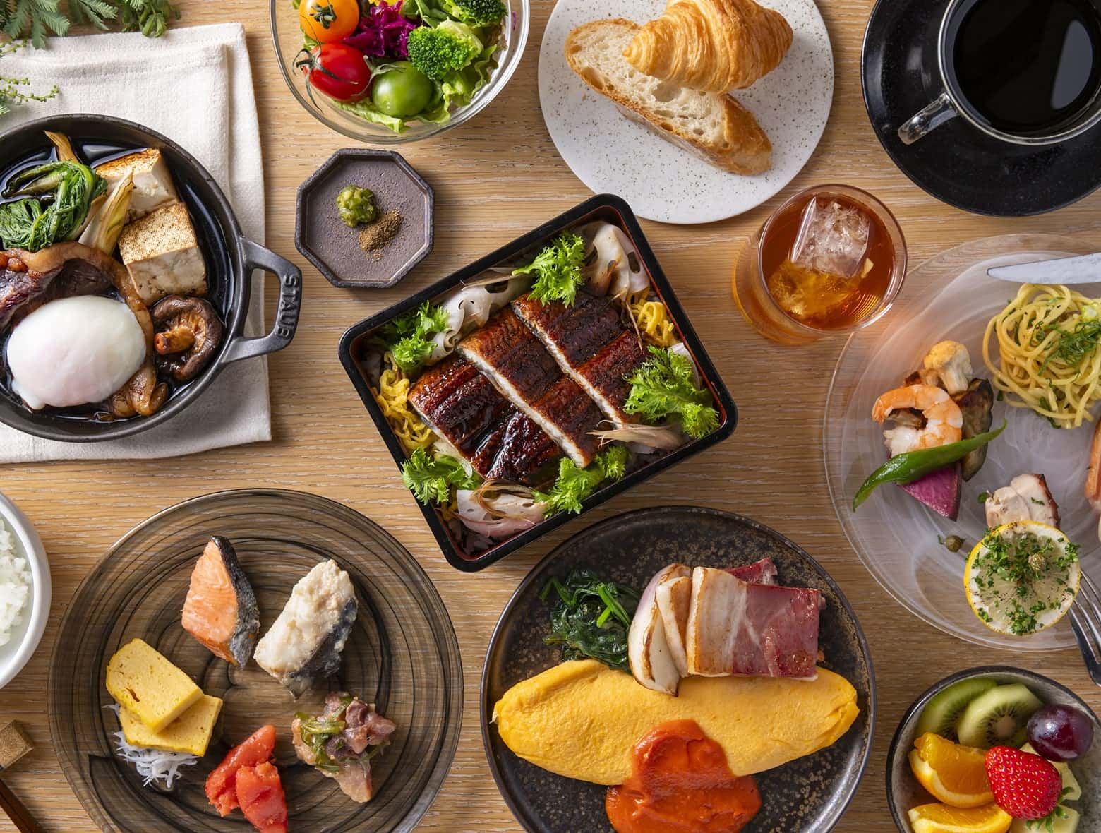 장어구이, 오믈렛, 생선, 신선한 과일, 페이스트리, 커피, 일본 요리로 우드 테이블을 채운 다채로운 조식.