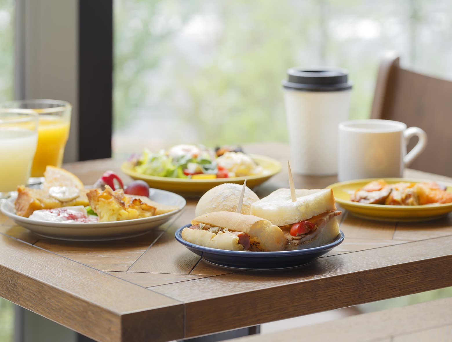 摆放在木桌上的早餐，包括三明治、果汁、糕点、沙拉和咖啡。