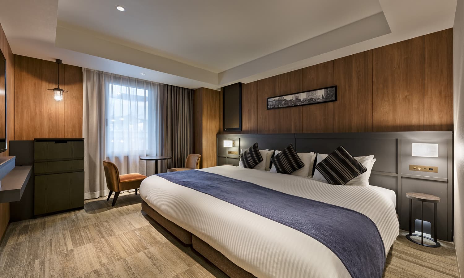 高级宽敞特大床房 - King配有一张加宽的特大床、木质镶板、一张带椅子的小桌和一台壁挂式电视。