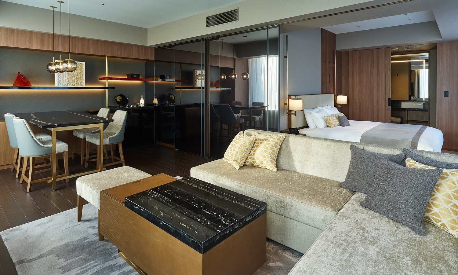 The Junior Suite, 1 bed King room includes a king-sized bed, L-shaped sofa, coffee table, dining table with chairs, espresso machine, and floating shelves with hidden lighting.
