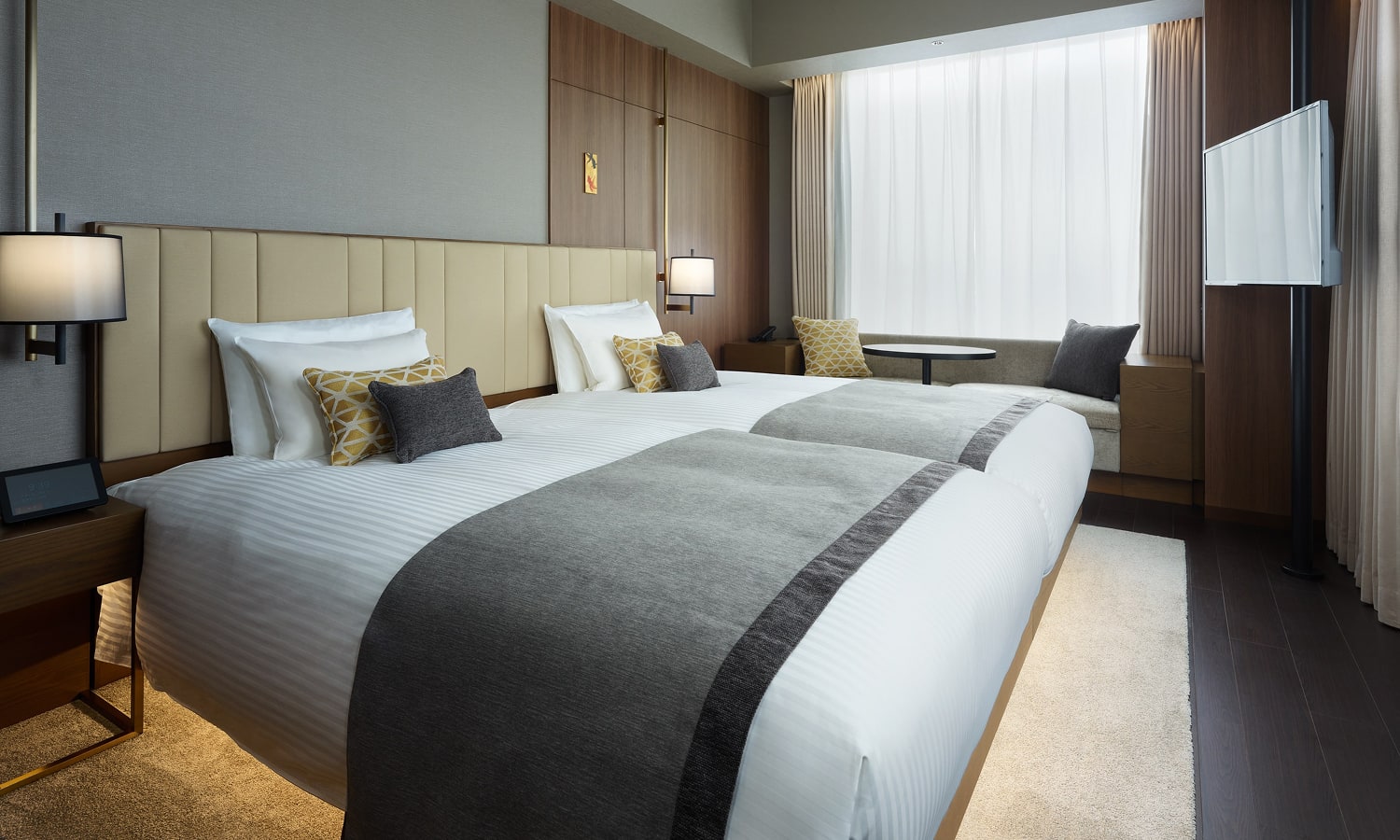The Deluxe, 2 beds (Hollywood-Style) room includes two side-by-side beds with padded headboards, a nightstand, an espresso machine, and a large window for natural light.