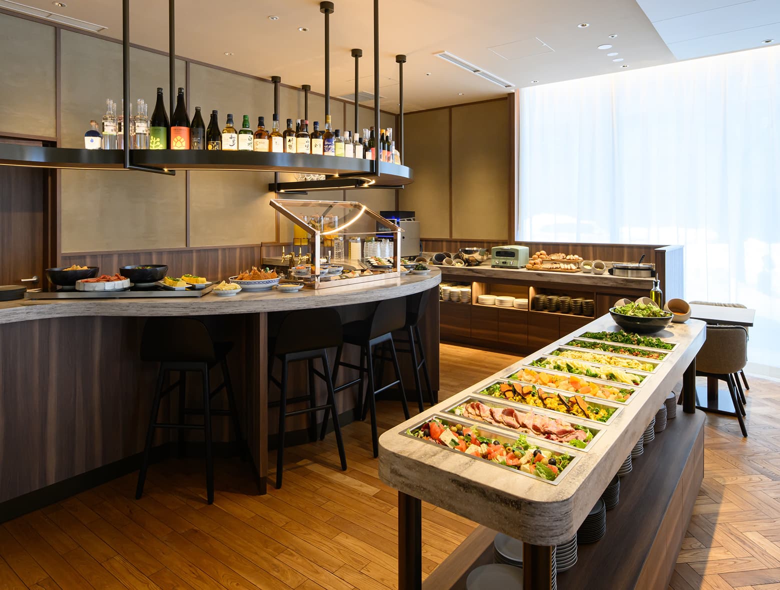 신선한 샐러드 바, 곡선형 서비스 카운터와 바 스툴, 다양한 병음료가 있는 현대적인 호텔 뷔페.