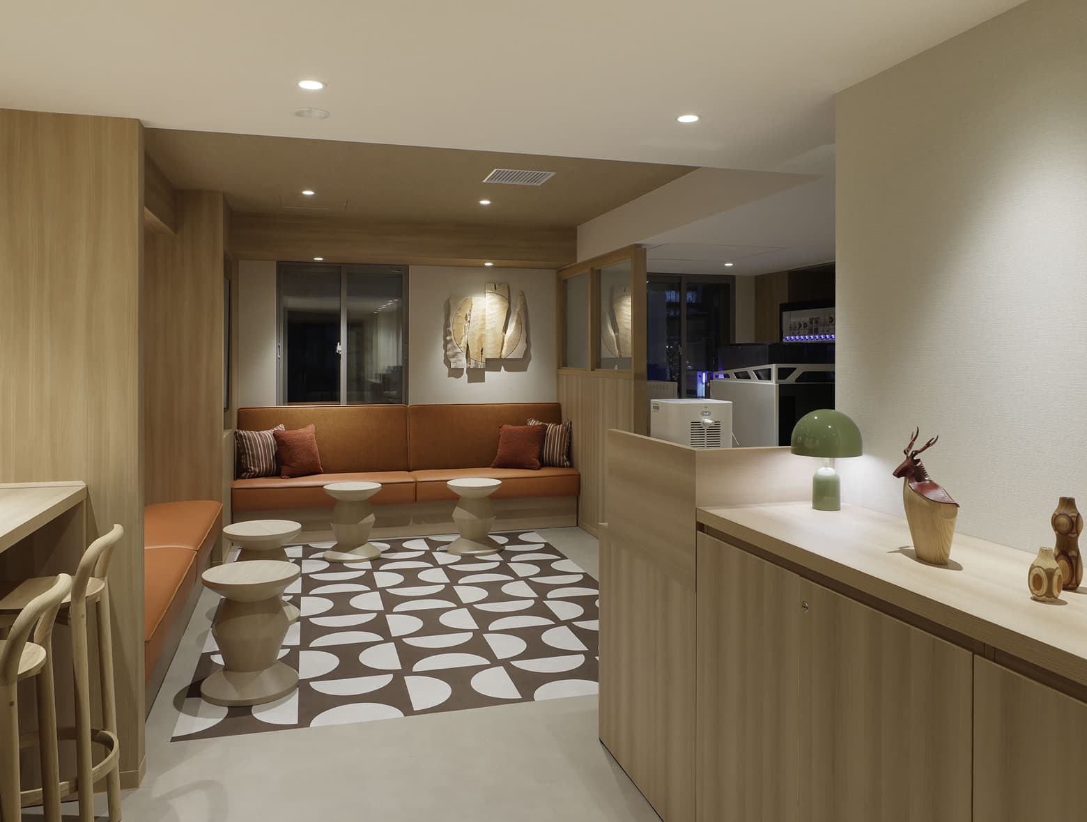 오렌지색 벤치형 좌석, 기하학적 무늬의 러그, 미니멀한 디자인의 스툴, 밝은 색 목재 수납장이 있는 현대적인 라운지.