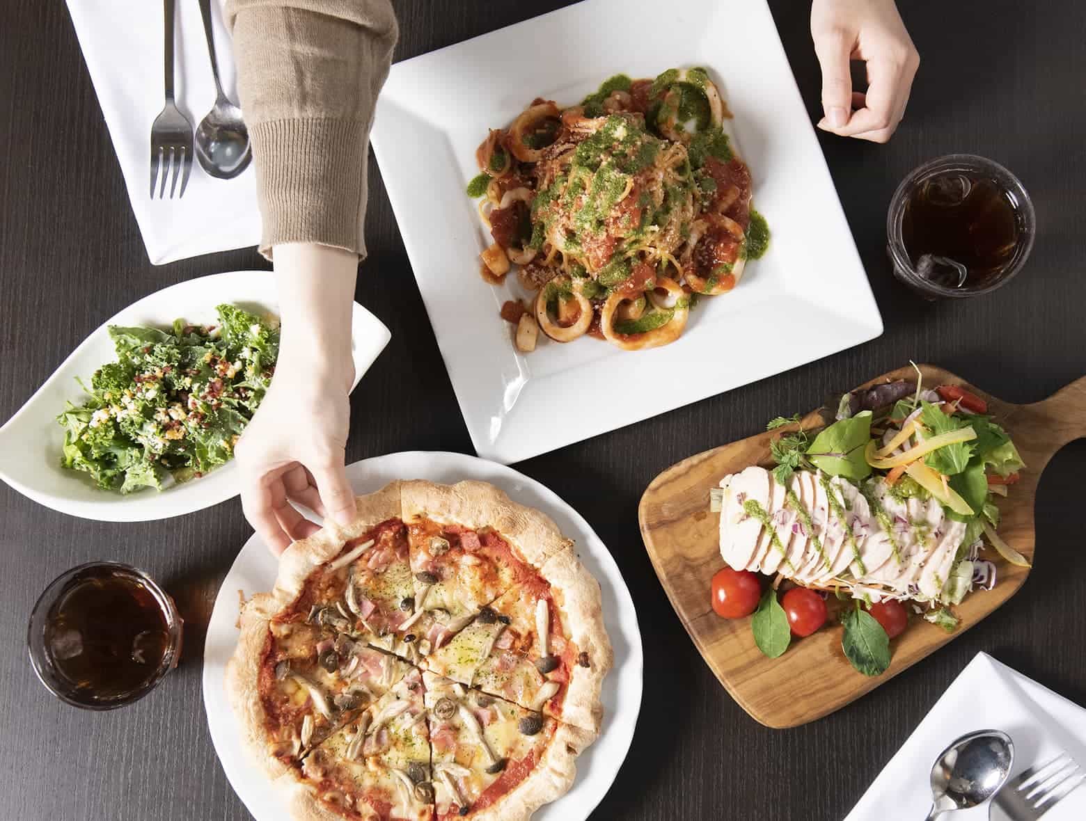 餐桌上擺放著各式菜餚,包括披薩、義大利麵和沙拉。