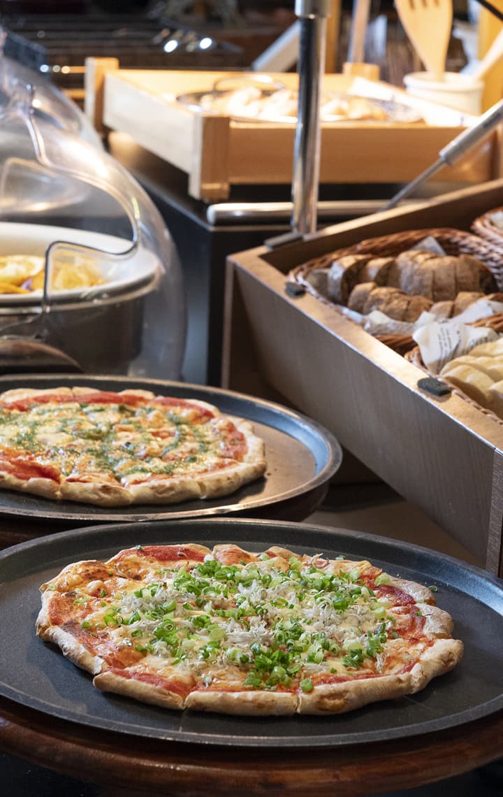 自助餐台上展示著披薩、編織籃中的各式麵包,背景是盛裝熱食的容器。