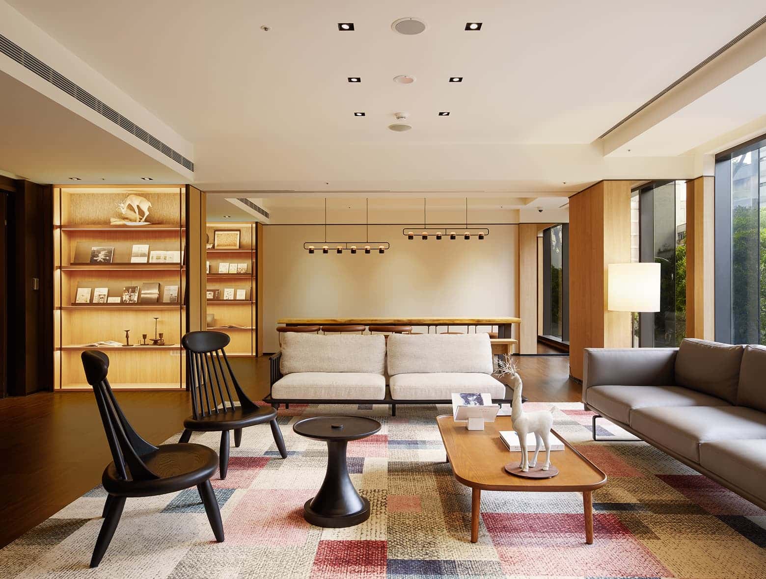 따뜻한 조명 아래 편안한 좌석, 다채로운 기하학적 무늬의 러그, 책장이 있는 현대적인 호텔 라운지.