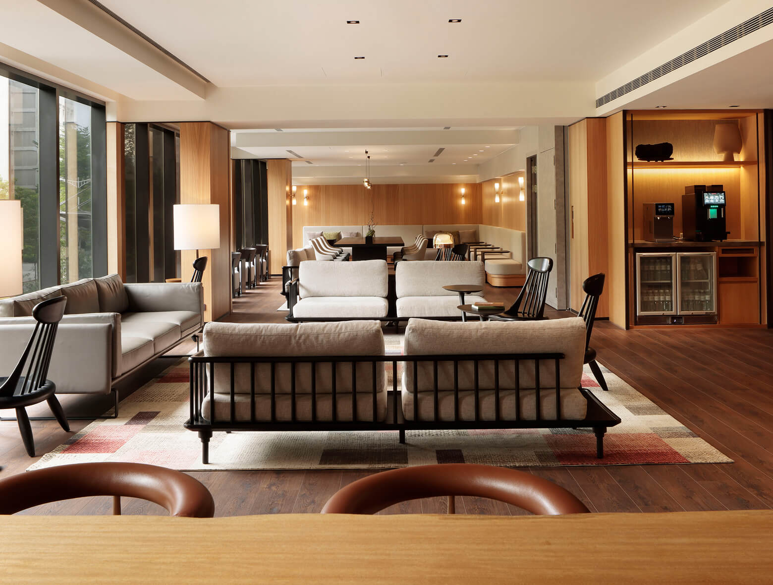 Modern hotel lounge with comfortable seating, a colorful geometric rug, and bookshelves under warm recessed lighting.