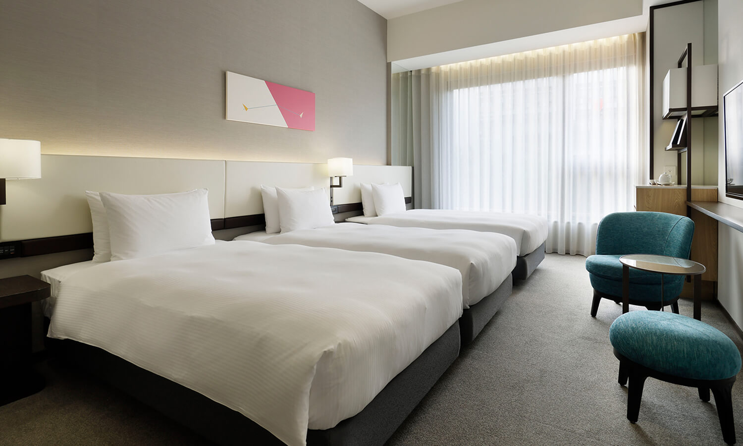 The Deluxe, 3 beds room features three twin beds, a blue and yellow geometric woven decoration above the headboard, a teal armchair, and large windows.