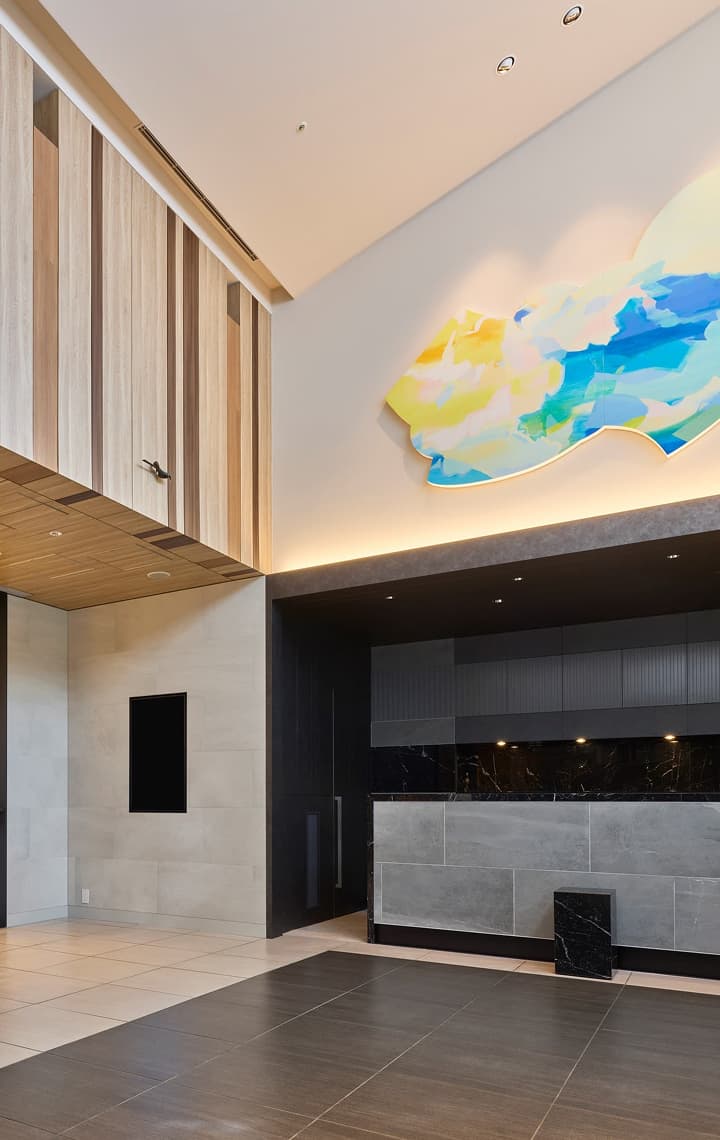 우드 패널 마감, 회색 석재 리셉션 데스크, 벽에 걸린 다채로운 예술 작품이 돋보이는 모던하고 미니멀한 호텔 로비.