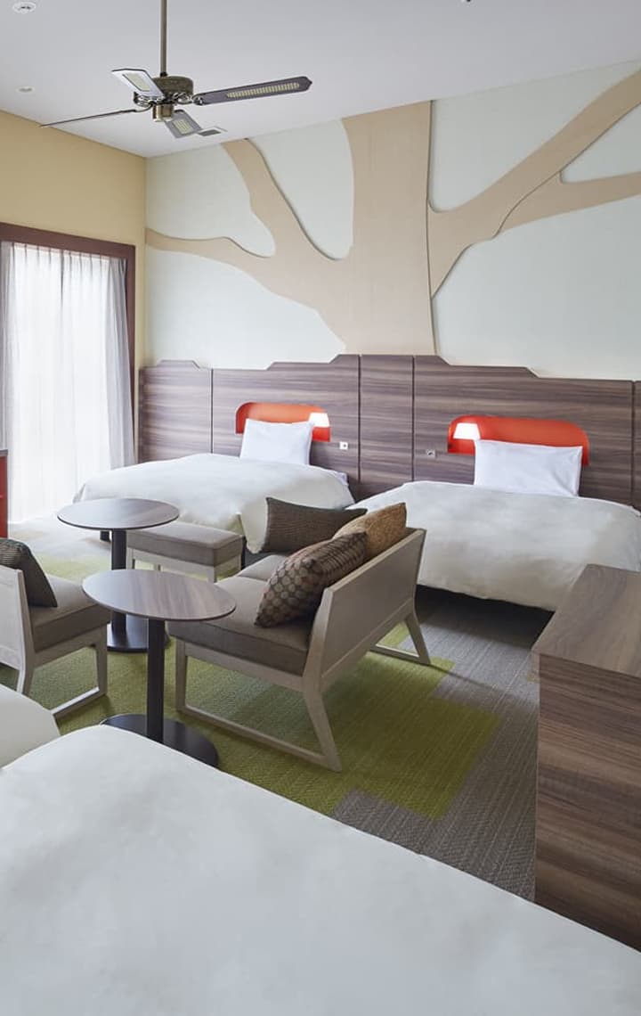 The Deluxe, 4 beds, Balcony room features four single beds, a pink accent wall, a large window for natural lighting, and a patterned carpet.