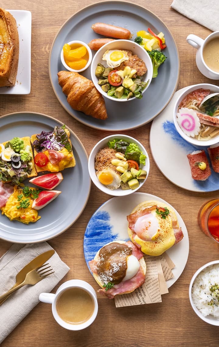 An overhead view of a large and diverse buffet spread featuring scrambled eggs, bacon, honey toast, pancakes, burgers, and Japanese items.